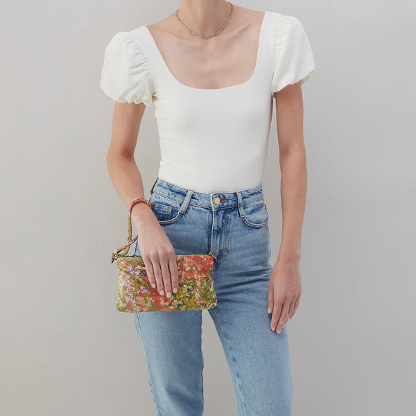 A Model Carrying a HOBO Darcy in Tropic Floral Printed Leather as a wristlet with the single solid leather strap.