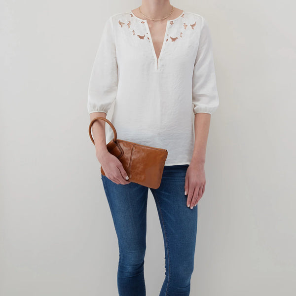 A model holding a HOBO Sable Wristlet Crafted in Natural Polished Leather. Her hand in on the bottom of the bag as to use with like a clutch with her arm going through the circular handle.